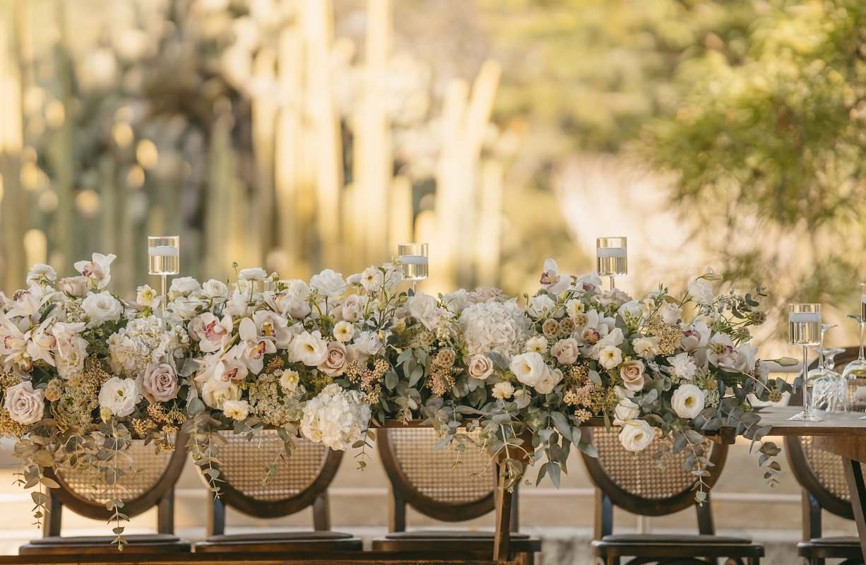 Rattan chairs behind a long runner of blush and cream roses in golden light