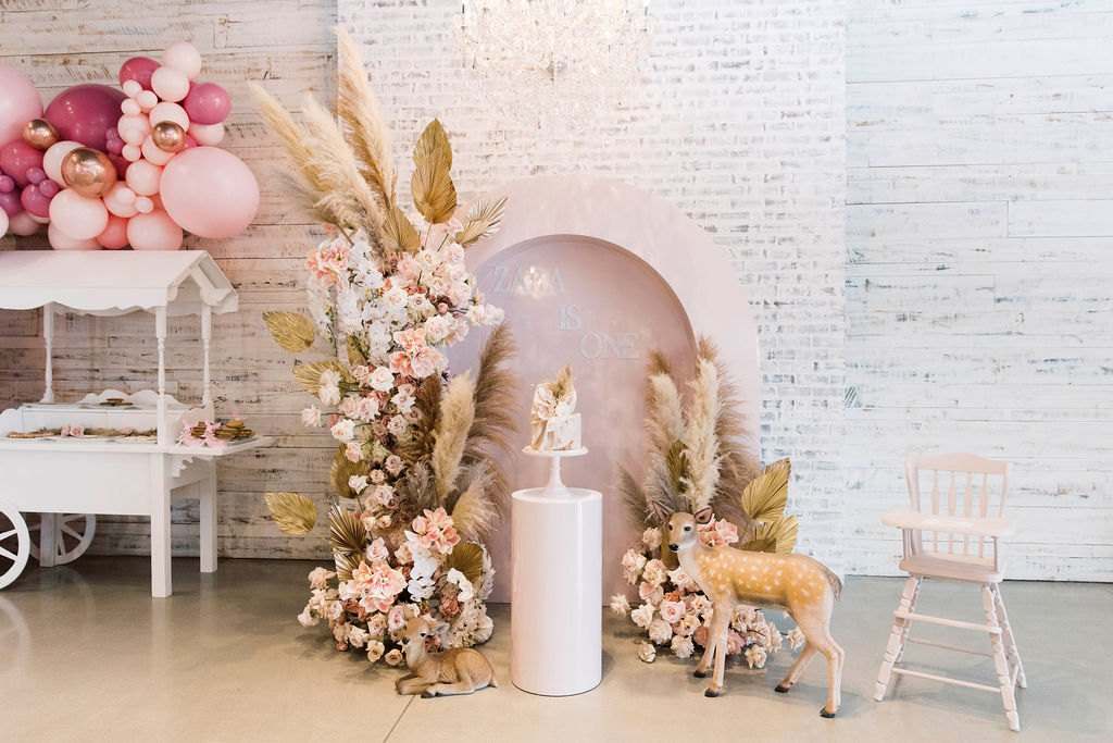 Baby shower corner with pampas grass, blush florals, a white arch and a high chair