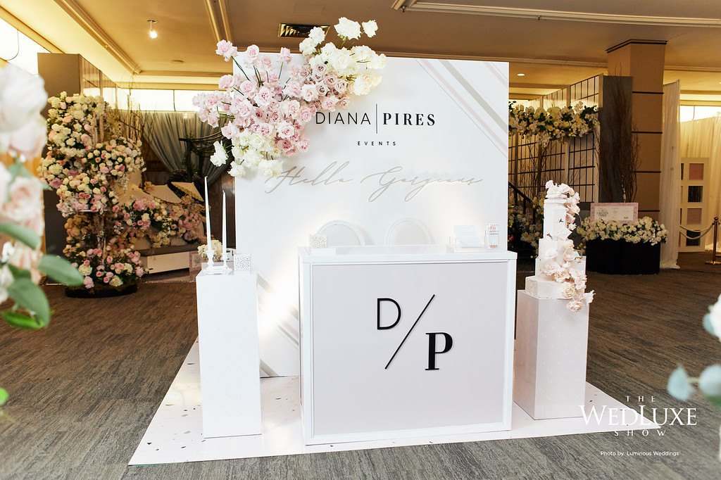 White brand booth with a monogram plinth, cake and blush florals