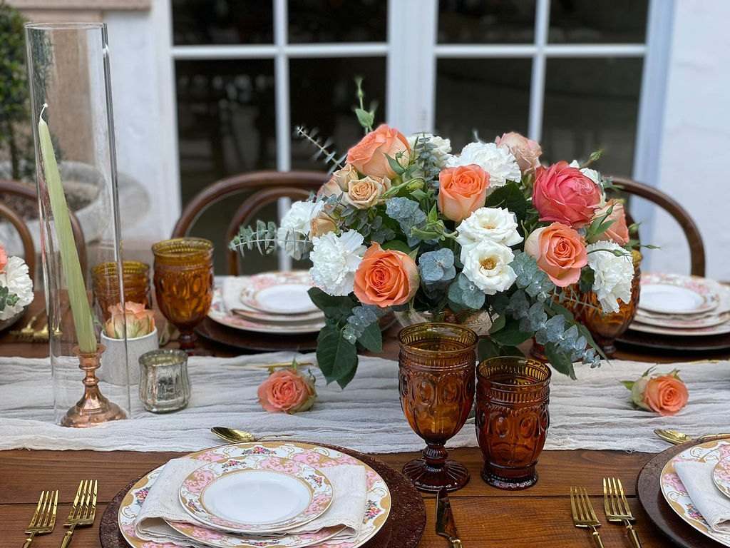 Coral roses in amber glass with patterned china by arched windows
