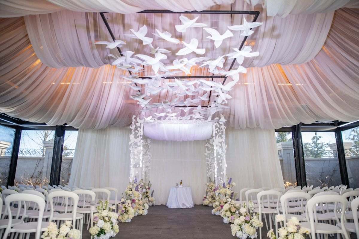 Draped blush ceremony room with a suspended white dove installation
