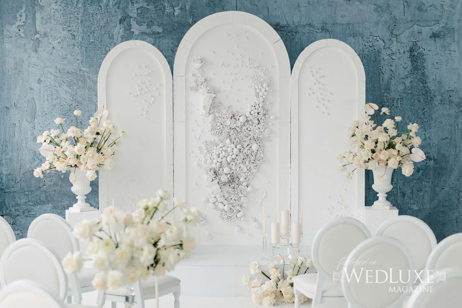 White sculpted panels with florals and white chairs against a blue wall