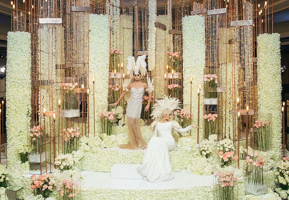Bride between tall columns of white flowers and gold frames
