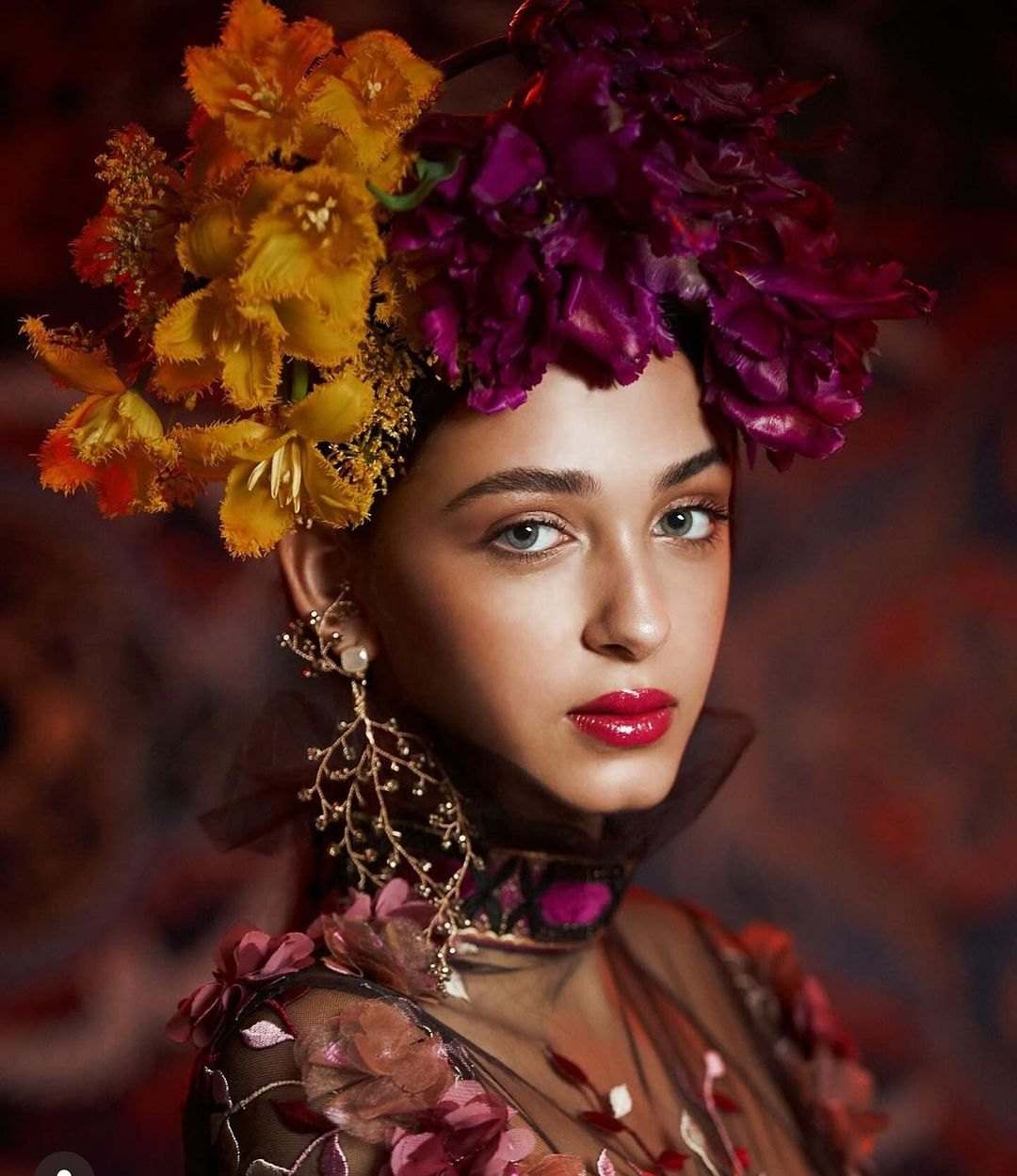 Portrait of a model wearing an oversized headpiece of burgundy and yellow flowers