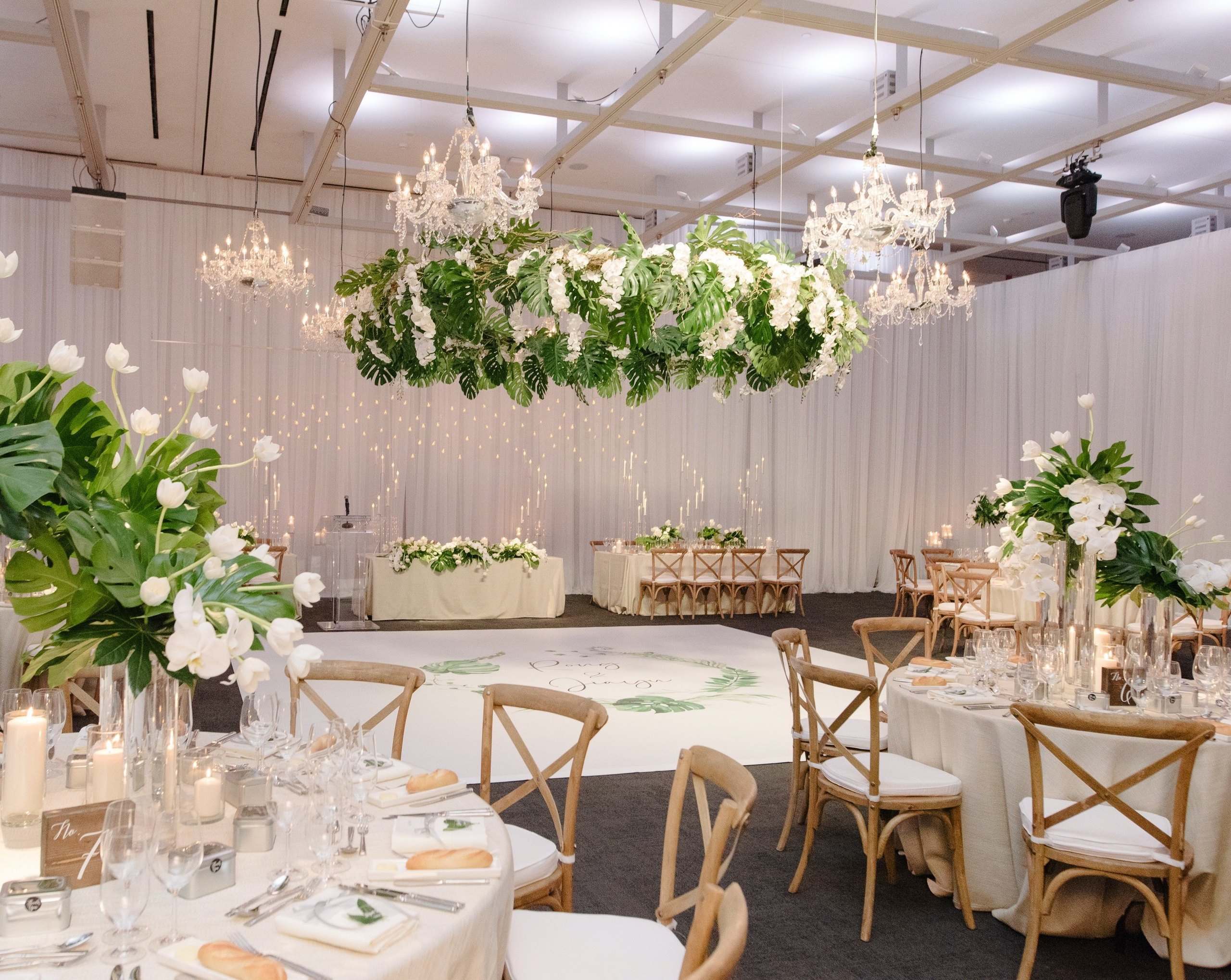Draped white hall with a suspended greenery ring and crystal chandeliers