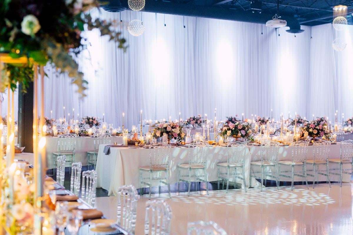 Long reception table in a hall draped in white with low florals