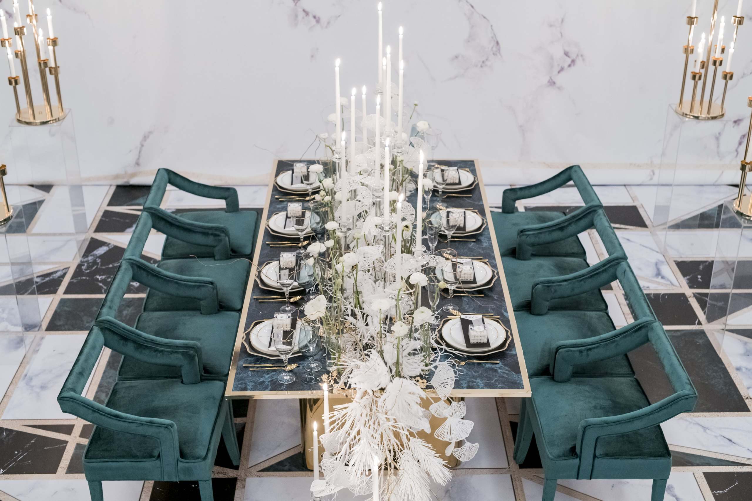 Teal velvet chairs around a marble banquet table with white florals and candles