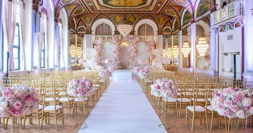 Gilded palace hall ceremony with gold chairs and pink floral pillars