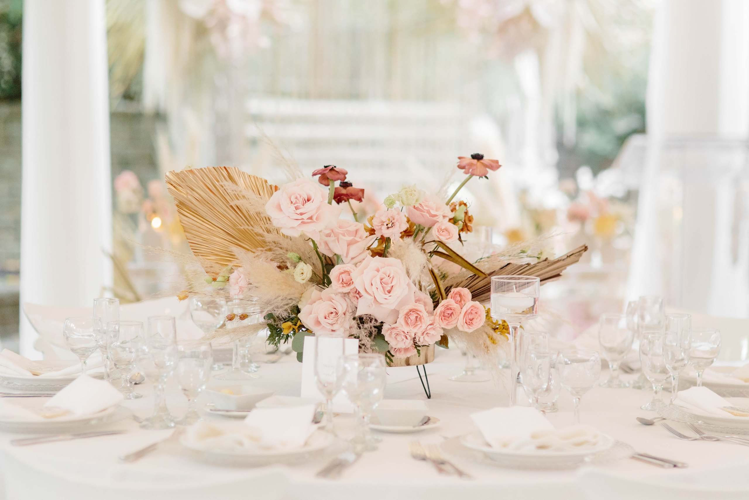 Pale roses and a gilded palm leaf centerpiece in a white room
