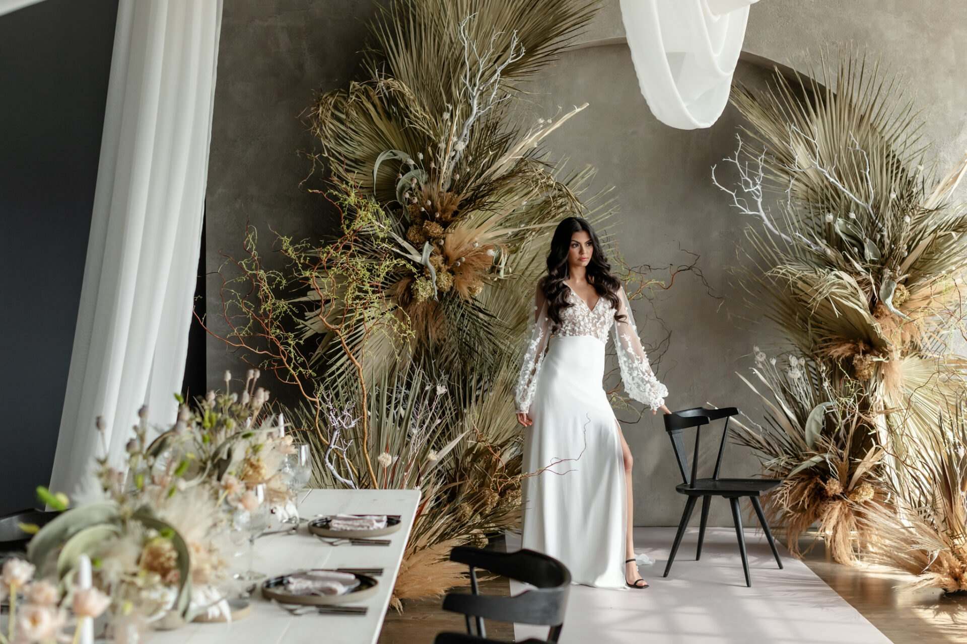 Bride beside a dried palm installation in a dark loft