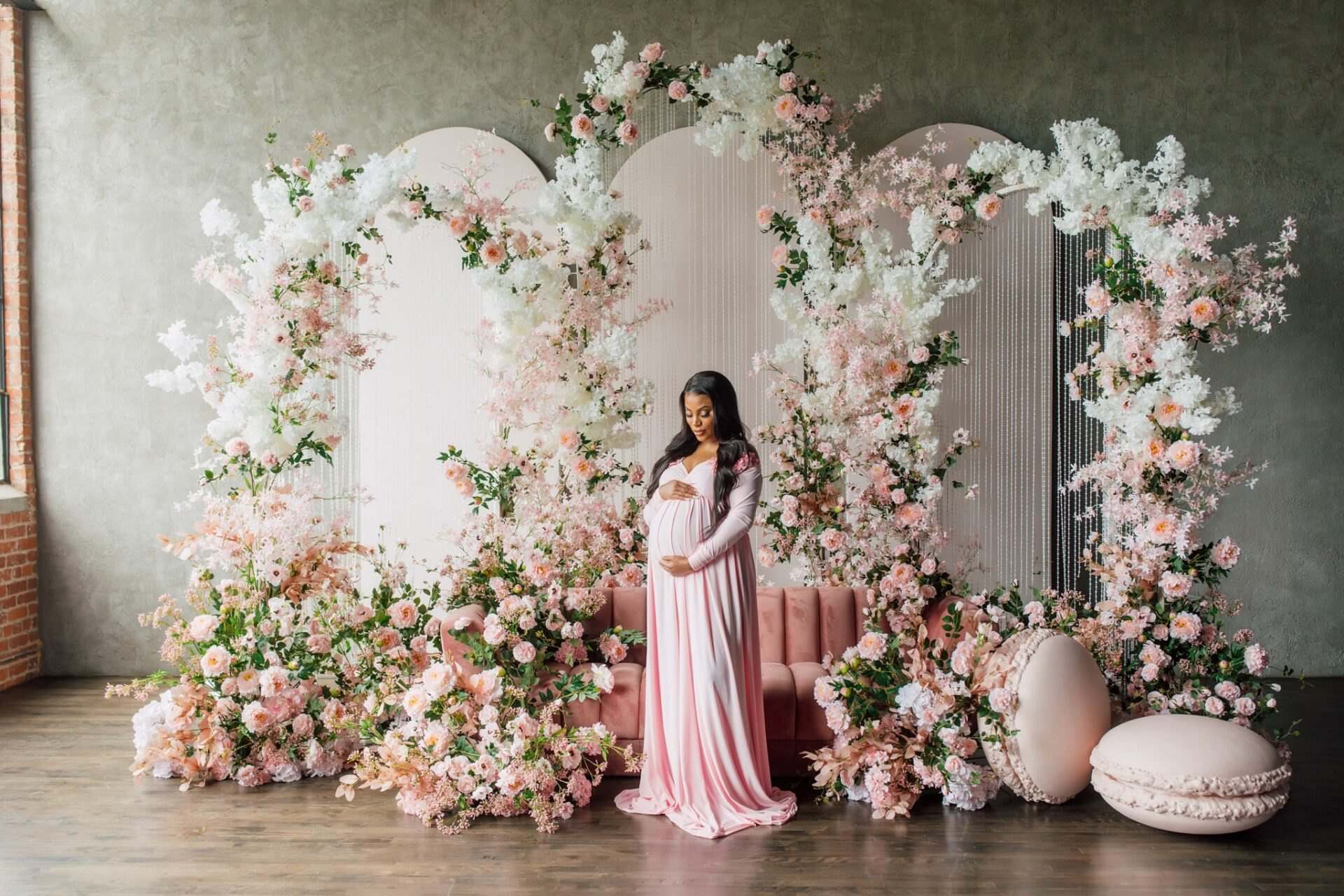 Expecting mother in pink before white arches covered in blush flowers