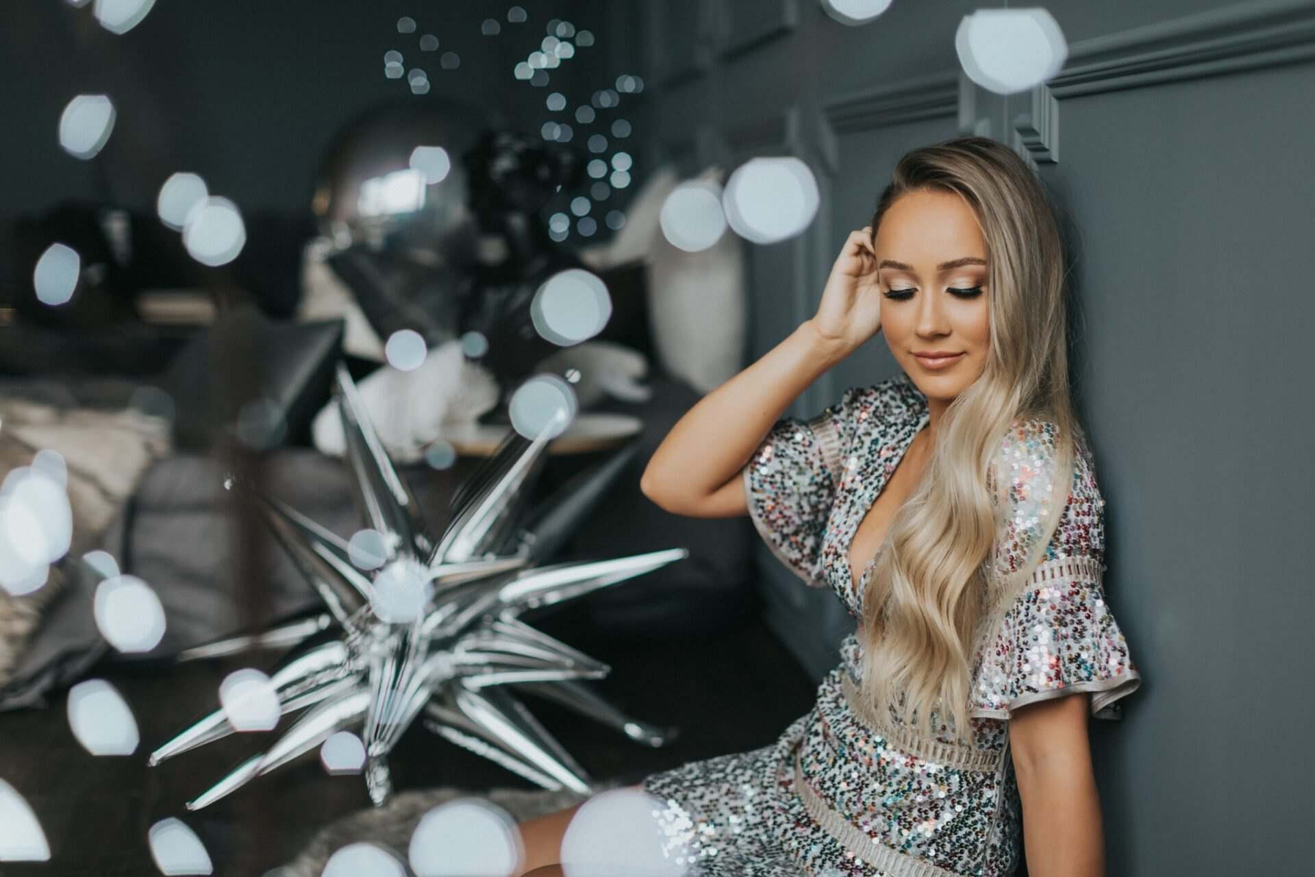 Woman in a sequin dress with silver star balloons and bokeh lights