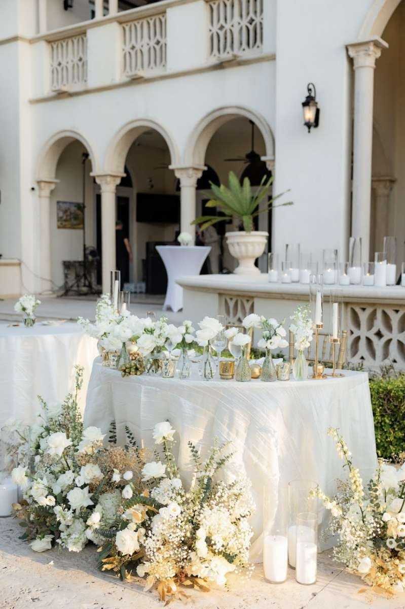 White sweetheart table with small vases of white flowers at a villa terrace