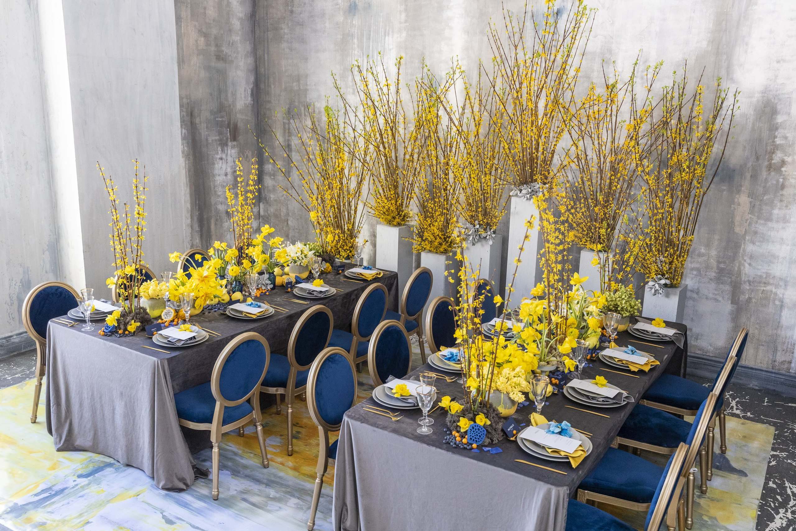 Yellow orchids on tall white vases along a grey banquet with navy chairs